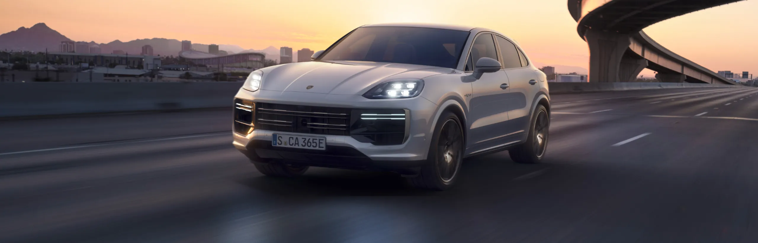 Una Porsche Cayenne Turbo E-Hybrid nel colore Bianco Carrara metallizzato che percorre una strada extraurbana. Vista frontale e laterale.