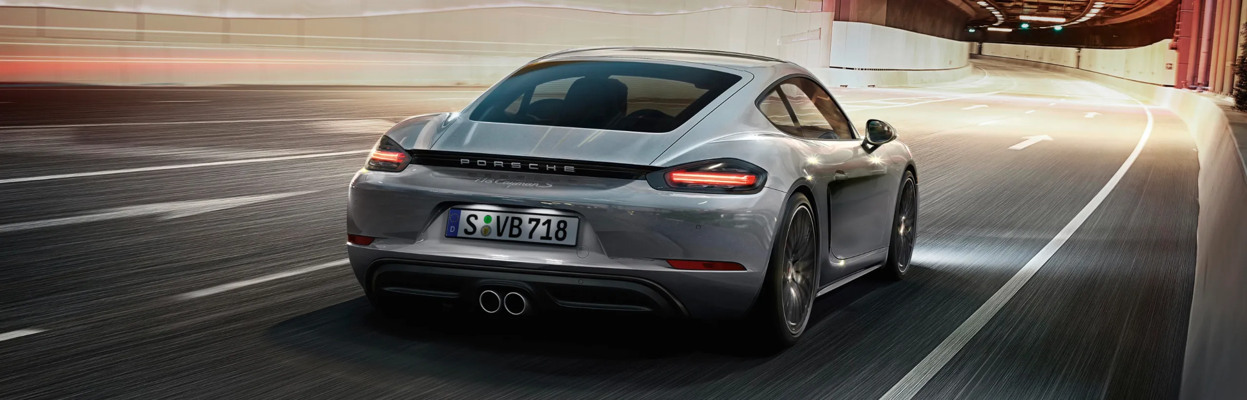 Porsche 718 Boxster S цвета синий металлик (Gentian Blue Metallic) проходит поворот на горной дороге. Вид на заднюю часть кузова.