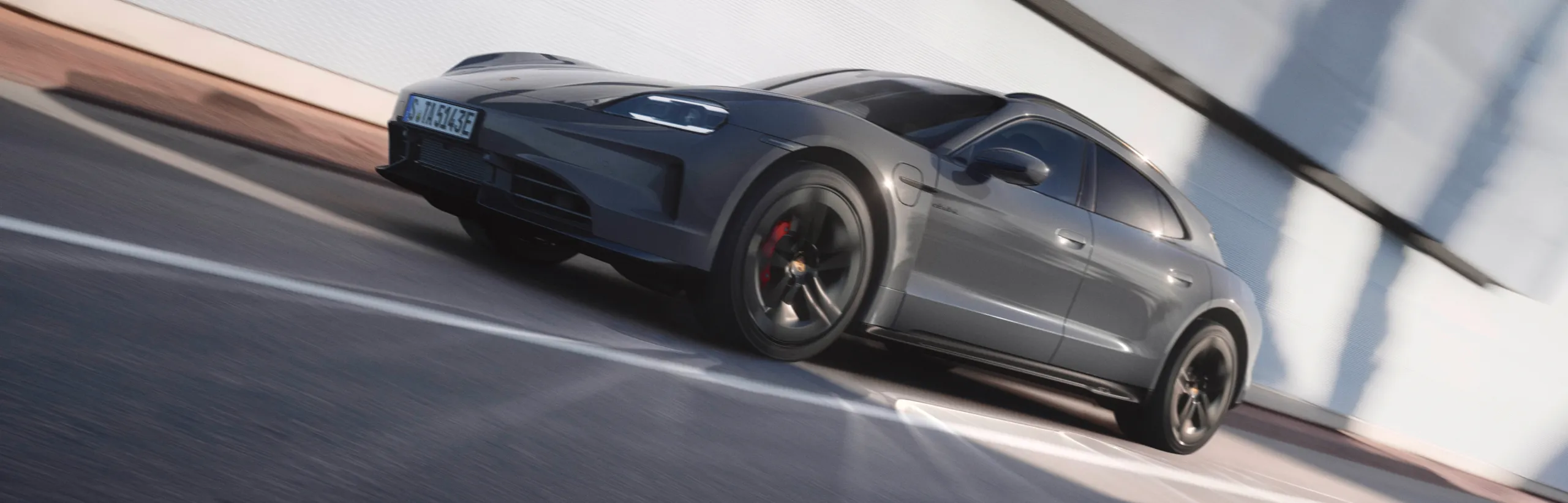 View of the front and side of a moving Porsche Taycan GTS Sport Turismo in Slate Grey Neo.