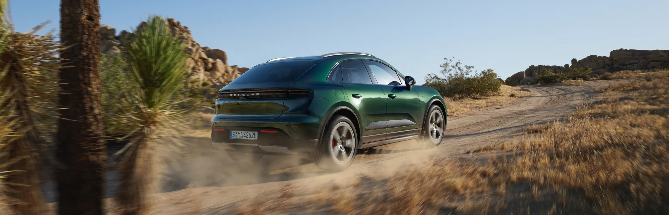 Porsche Macan 4S in Oakgrünmetallic fährt durchs Gelände. Front und Seite sichtbar.