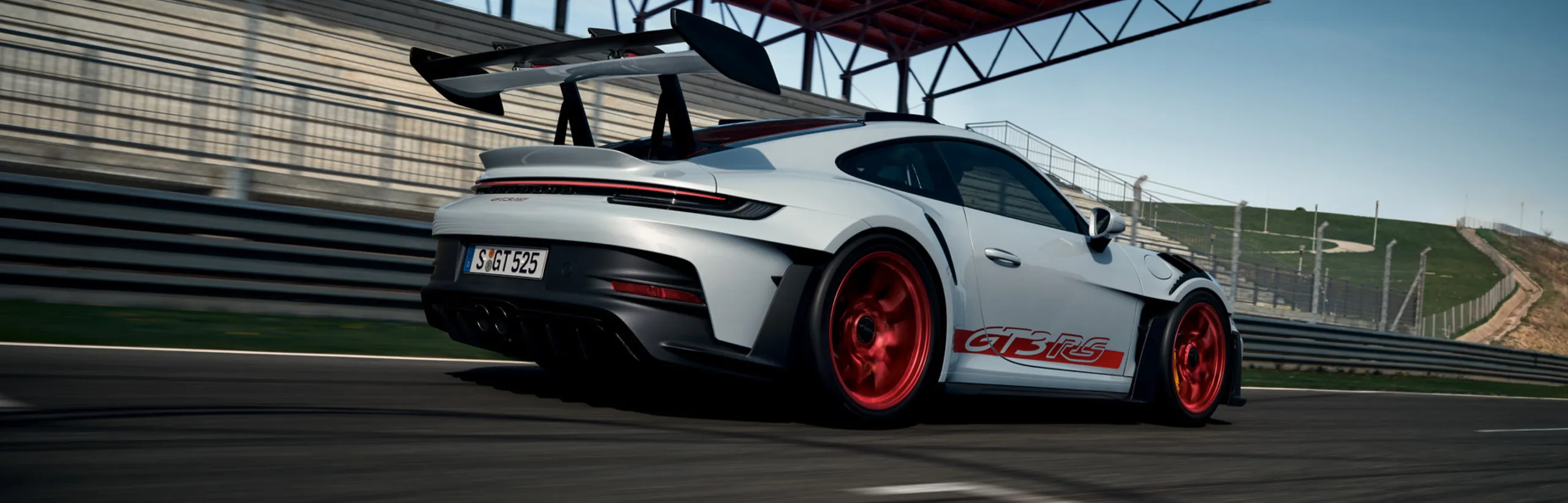 The Porsche 911 GT3 RS in Ice Grey Metallic driving on a rack track. Rear and side view.