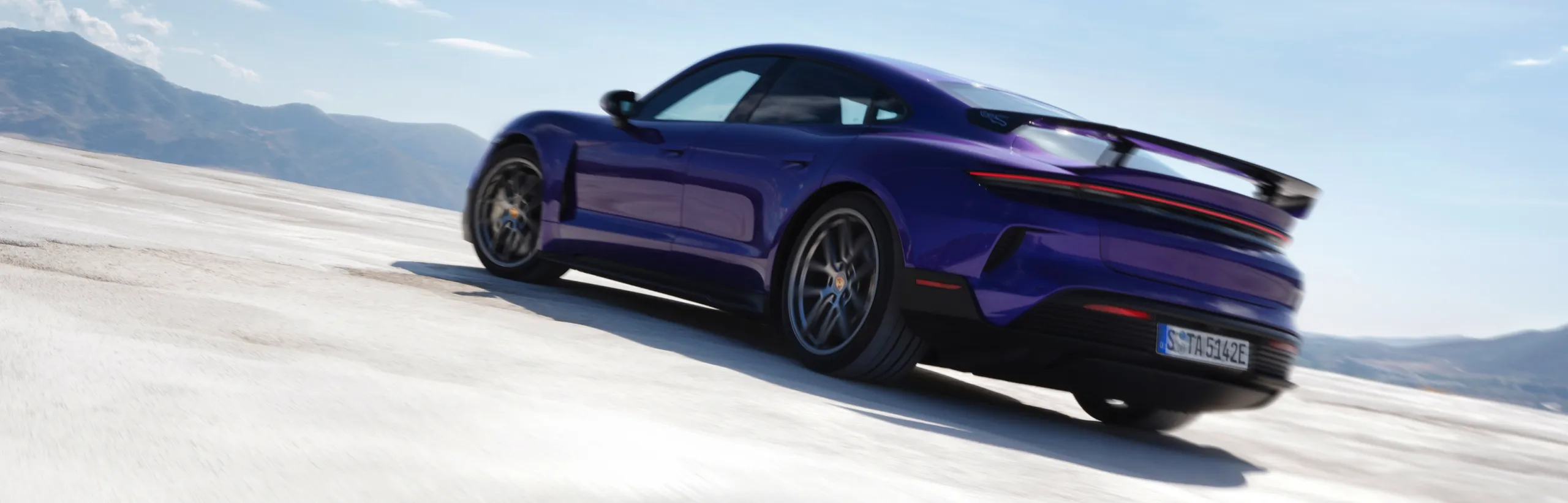 Porsche Taycan Turbo GT mit Weissach-Paket in Purpleskymetallic fährt über Salzsee. Blick auf Heck und Seite.