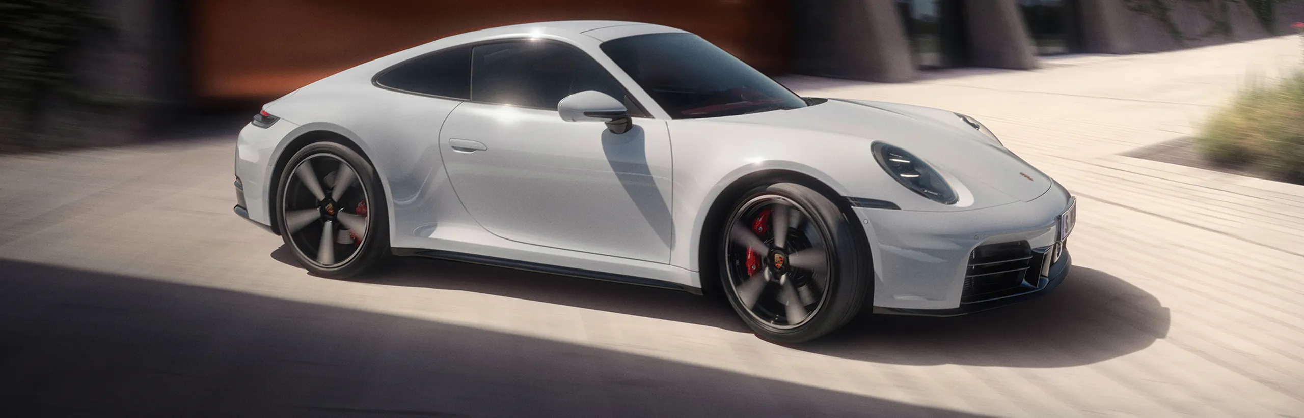 Un Porsche 911 Carrera GTS en color Gris Pizarra Neo circulando por una carretera. Vista desde delante de la parte delantera.