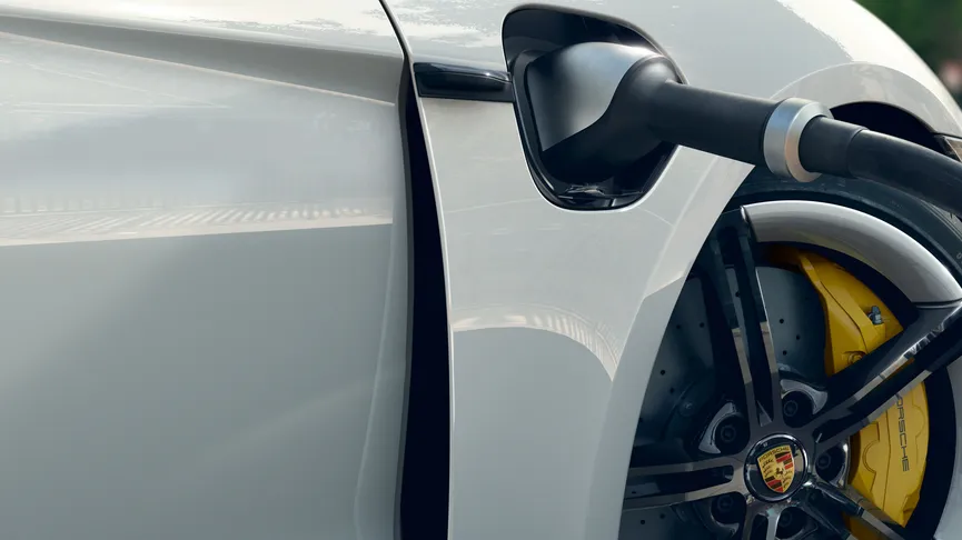 Close-up of a white electric car being charged, focusing on the charging port and wheel with yellow brake calipers.