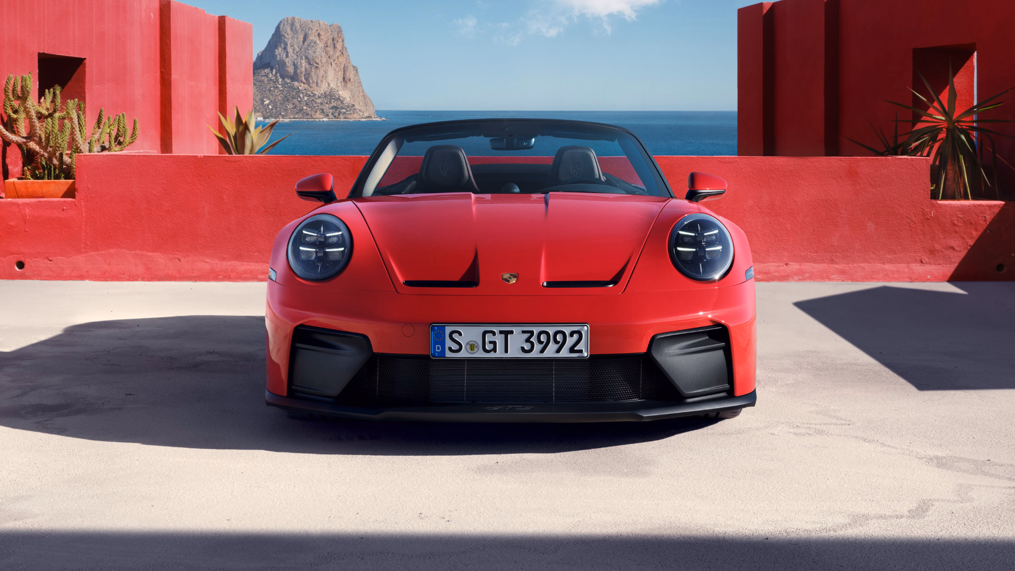 Front view of a Porsche 911 GT3 S/C in Guards Red in front of various red-coloured concrete blocks. Sea in the background.