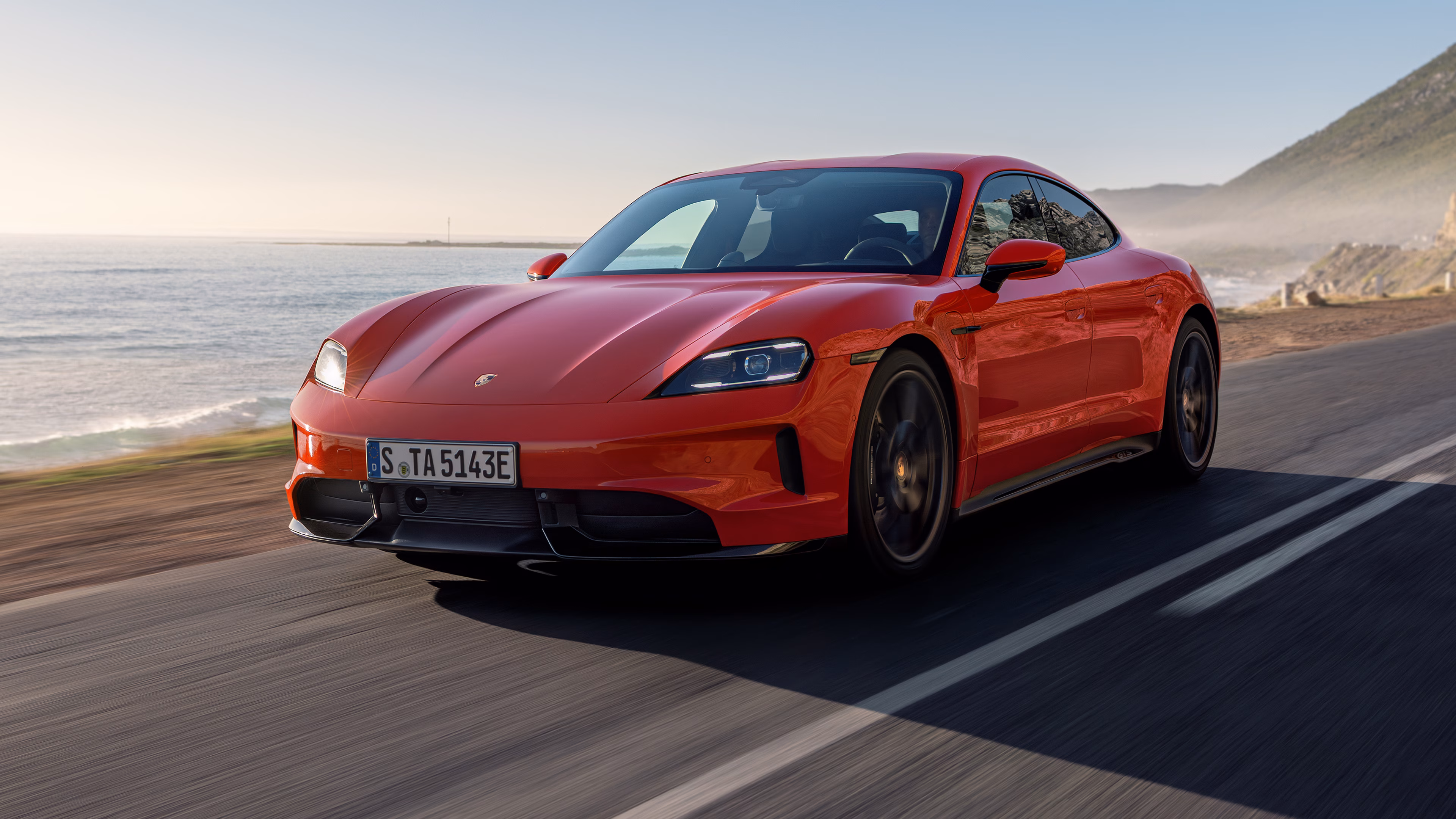 Front view of a moving Porsche Taycan GTS in Carmine Red.