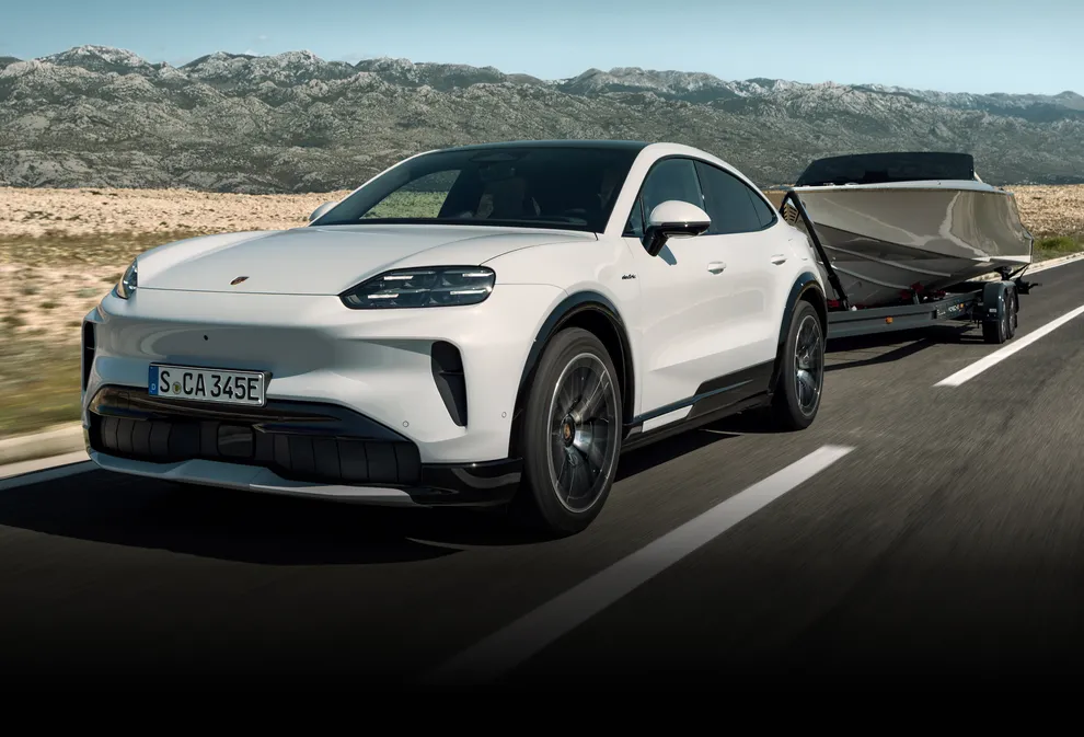 Ein Porsche Cayenne S Coupé in Carraraweißmetallic zieht ein Boot auf einem Anhänger.