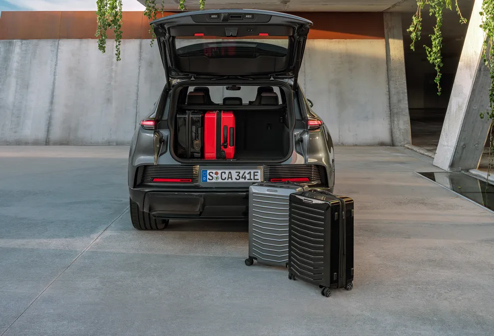 Blick von hinten auf einen Porsche Cayenne in Vanadiumgraumetallic mit geöffnetem Kofferraum. Darin und davor Koffer.