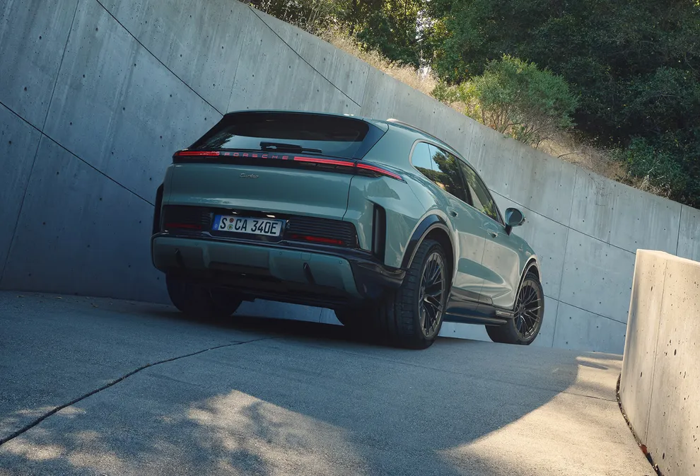 Blick von hinten auf einen Porsche Cayenne Turbo in Mysticgrünmetallic an einer kurvigen Auffahrt.
