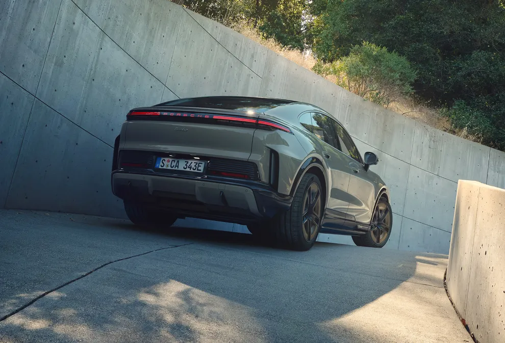 Blick von hinten auf einen Porsche Cayenne Turbo Coupé in Monteverdemetallic an einer kurvigen Auffahrt.