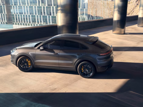 Porsche Cayenne Turbo E-Hybrid Coupé med GT-paket i Quarzite Grey Metallic står i stadsmiljö. Vy mot sidan.
