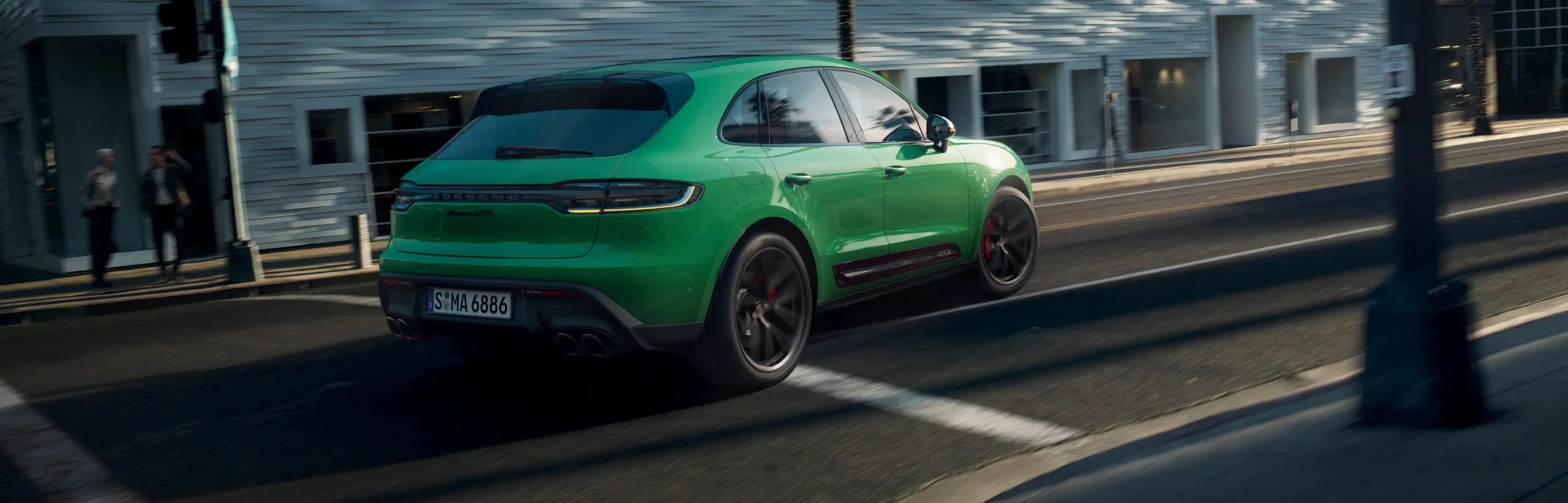 Un Porsche Macan GTS en color Verde Python circulando por la ciudad. Vista trasera y lateral.