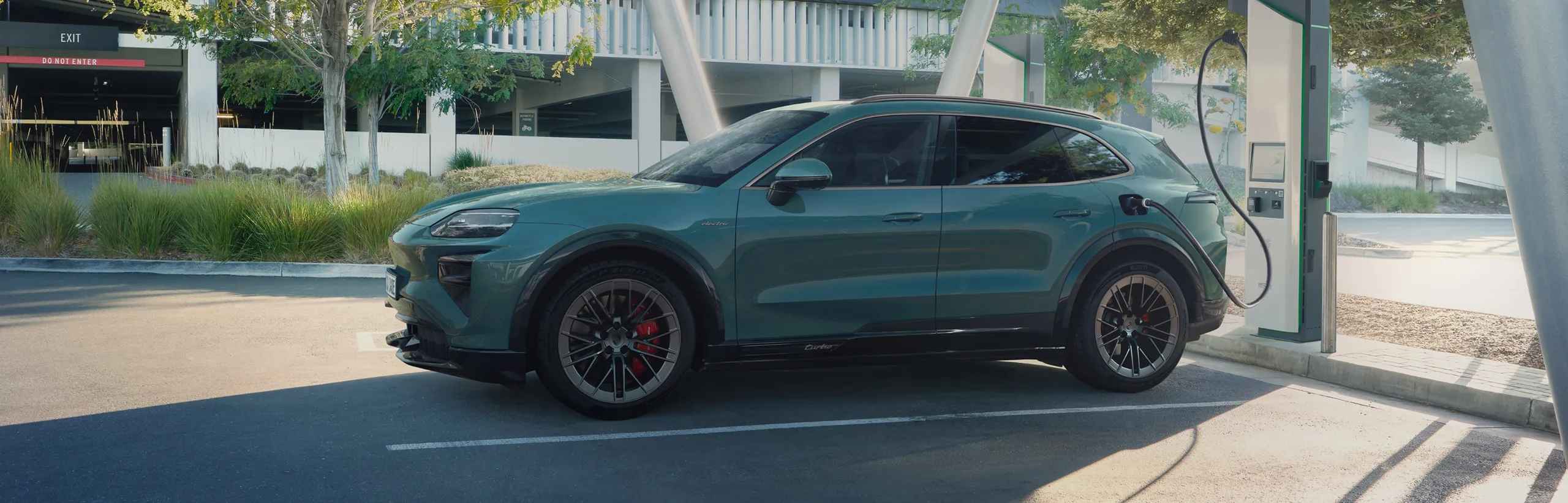 A Porsche Cayenne Turbo in Mystic Green Metallic charging at a charging pedestal.