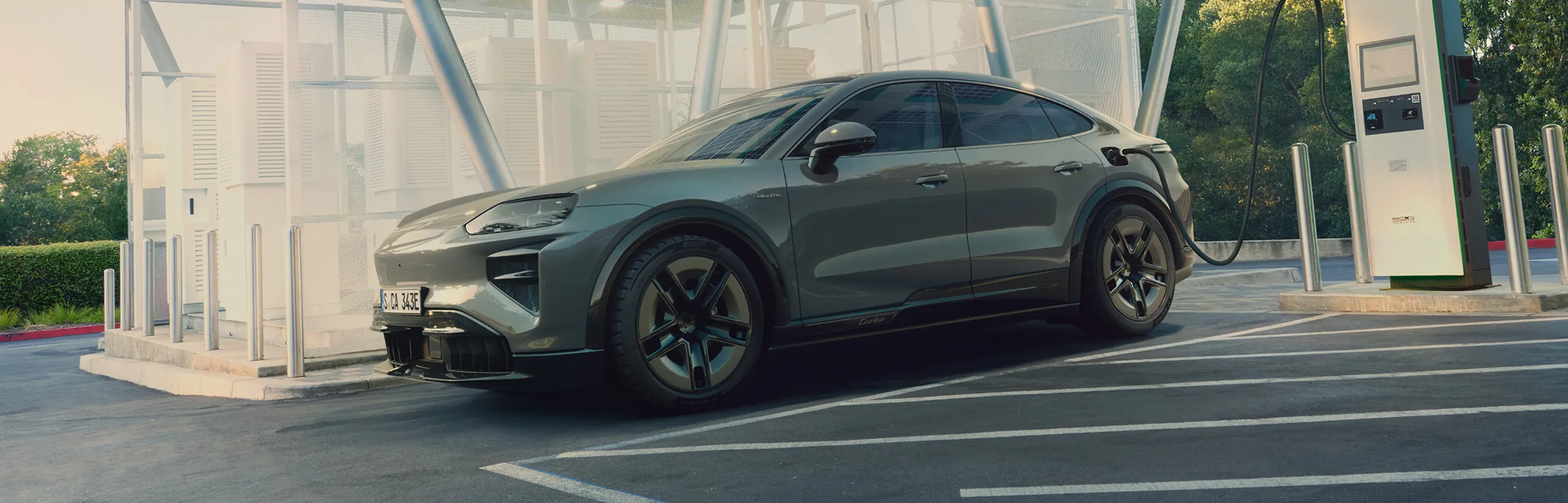 A Porsche Cayenne Turbo Coupé in Monteverde Metallic being charged at a charging pedestal.