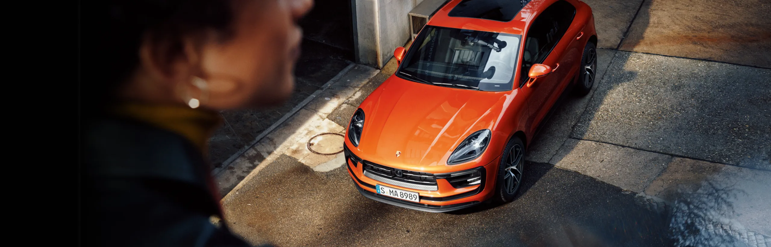 街の中のパパイヤメタリックのPorsche Macan S。上から見たフロントとルーフ。