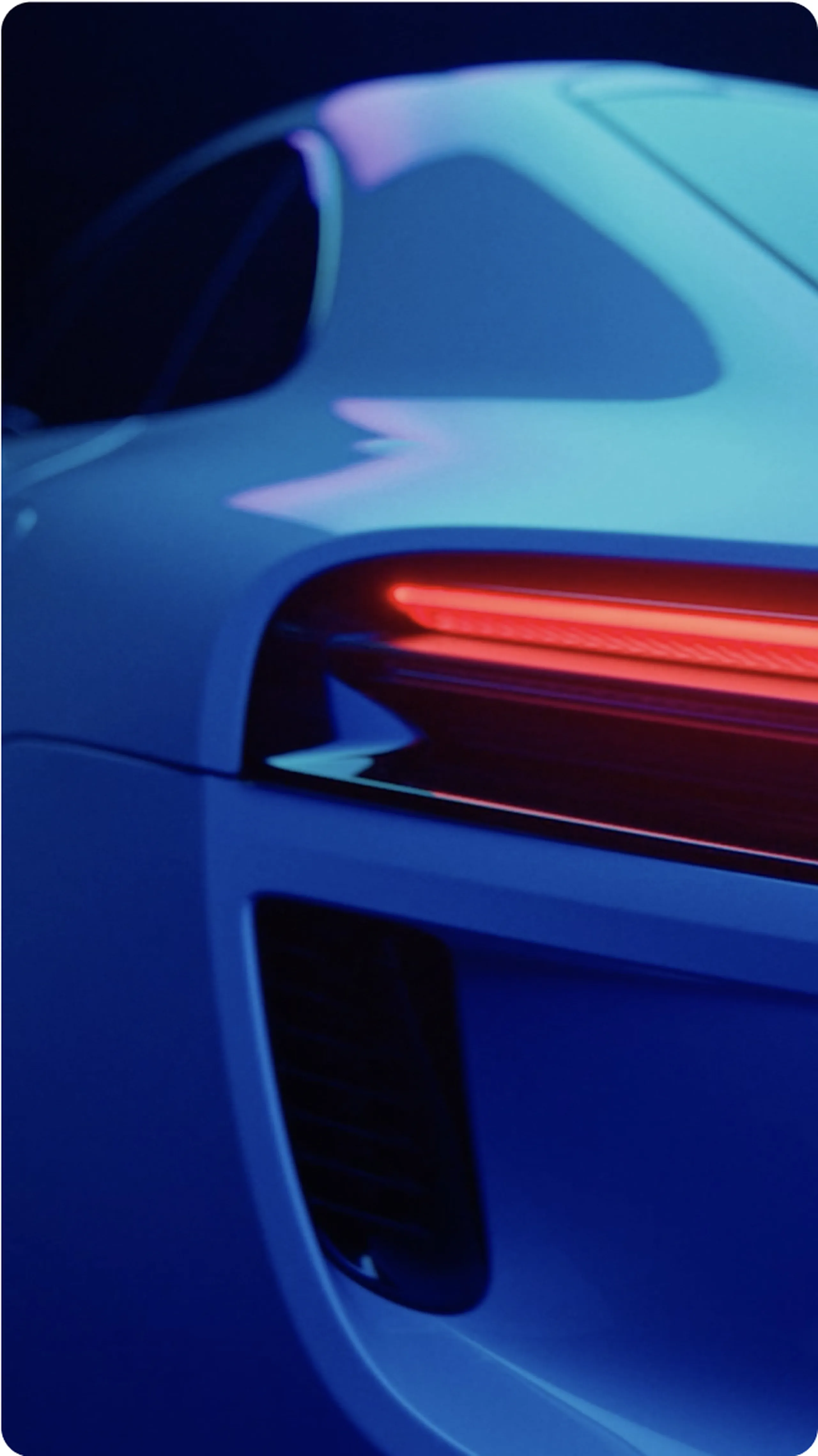 Close-up of a sleek, modern car's rear with illuminated red tail light, showcasing aerodynamic curves, in a dimly lit setting.