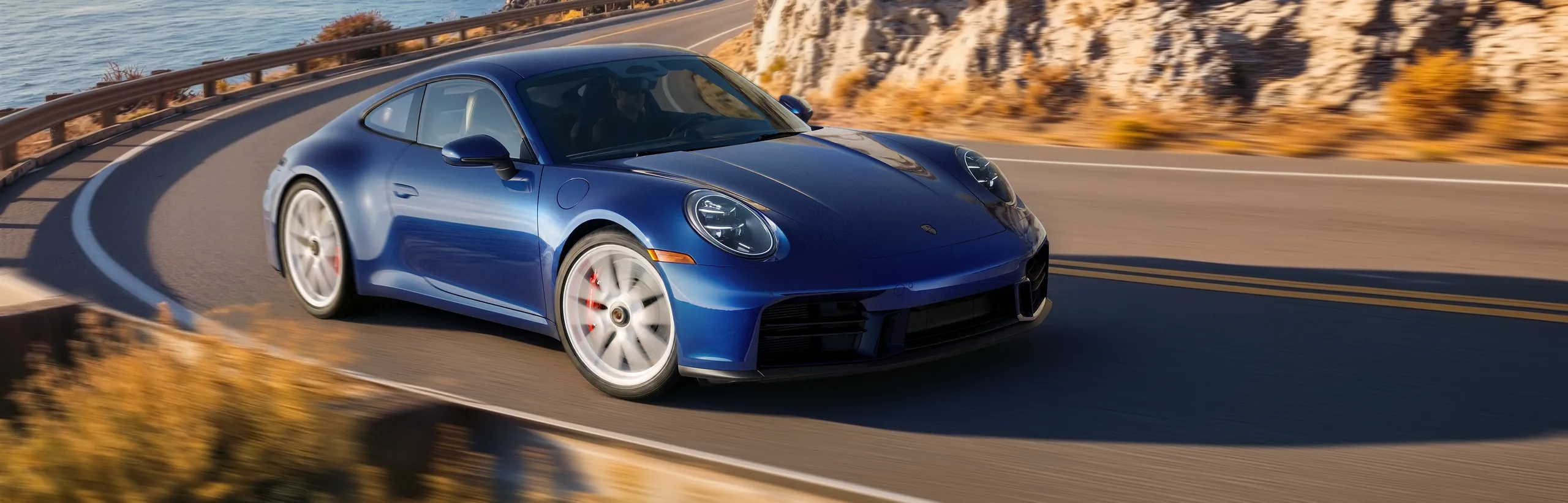 Porsche 911 Carrera S with MT-Package in gentian blue driving on a road. Front and side views.