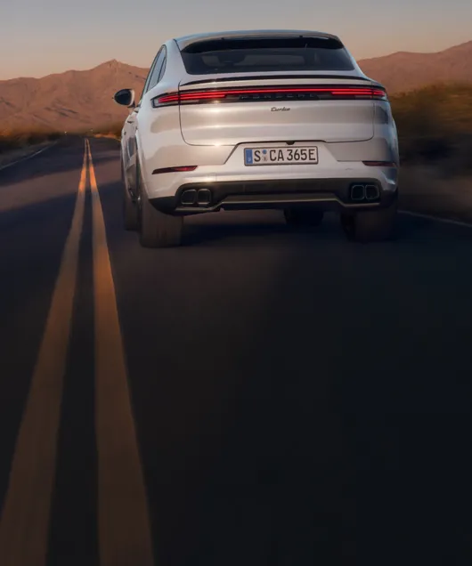 Porsche Cayenne Turbo E-Hybrid Coupé in Carraraweißmetallic fährt auf Straße. Blick von hinten aufs Heck.