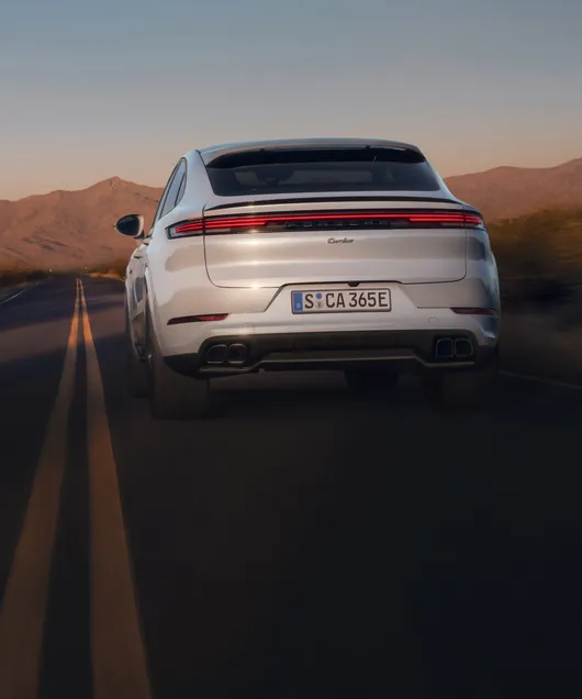 Porsche Cayenne Turbo E-Hybrid Coupé in Carraraweißmetallic fährt auf Straße. Blick von hinten aufs Heck.
