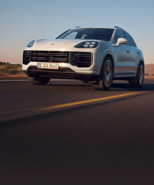 Le Porsche Cayenne Turbo E-Hybrid en Blanc Carrara métallisé roule sur une route de campagne. Vue de face et latérale.