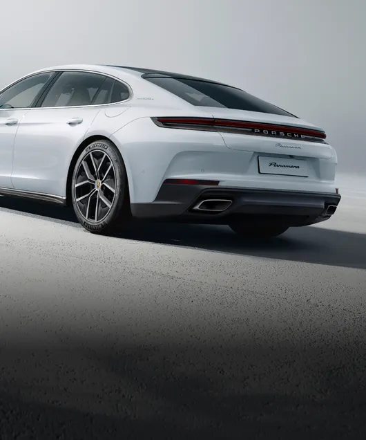 Porsche Panamera 4 E-Hybrid Executive in carrarawit metallic tegen een lichtgrijze achtergrond. Zicht van achteren op de achterkant en zijkant.