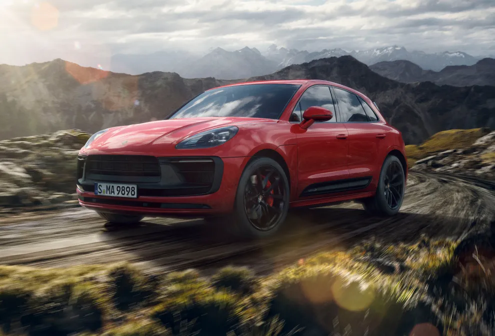 Porsche Macan GTS em Vermelho Carmim dirigindo por uma paisagem montanhosa. Vistas frontal e lateral.