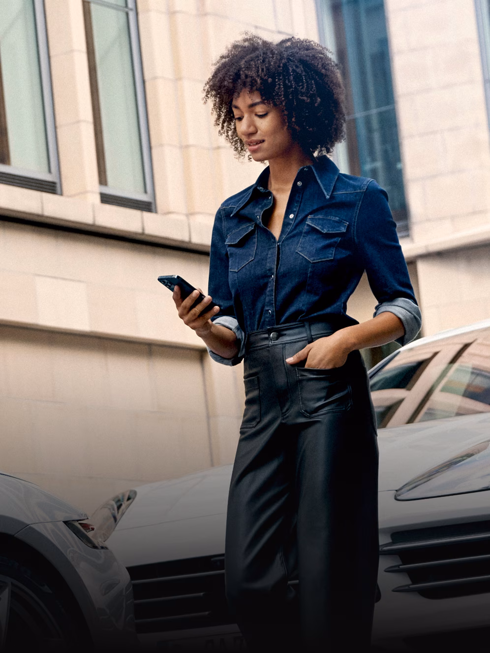 Woman looks at her smartphone. A white Porsche is in the background.