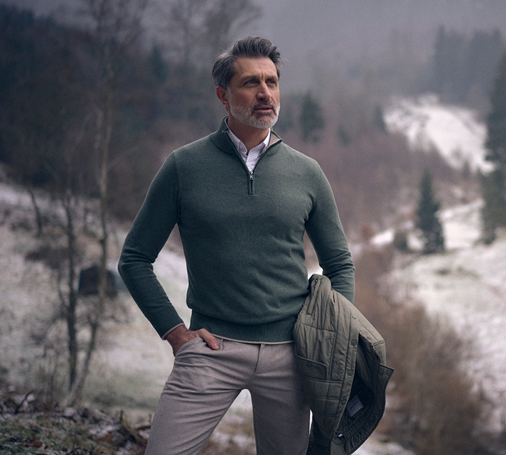 Man gekleed in een groene schipperstrui, wit overhemd en grijze broek