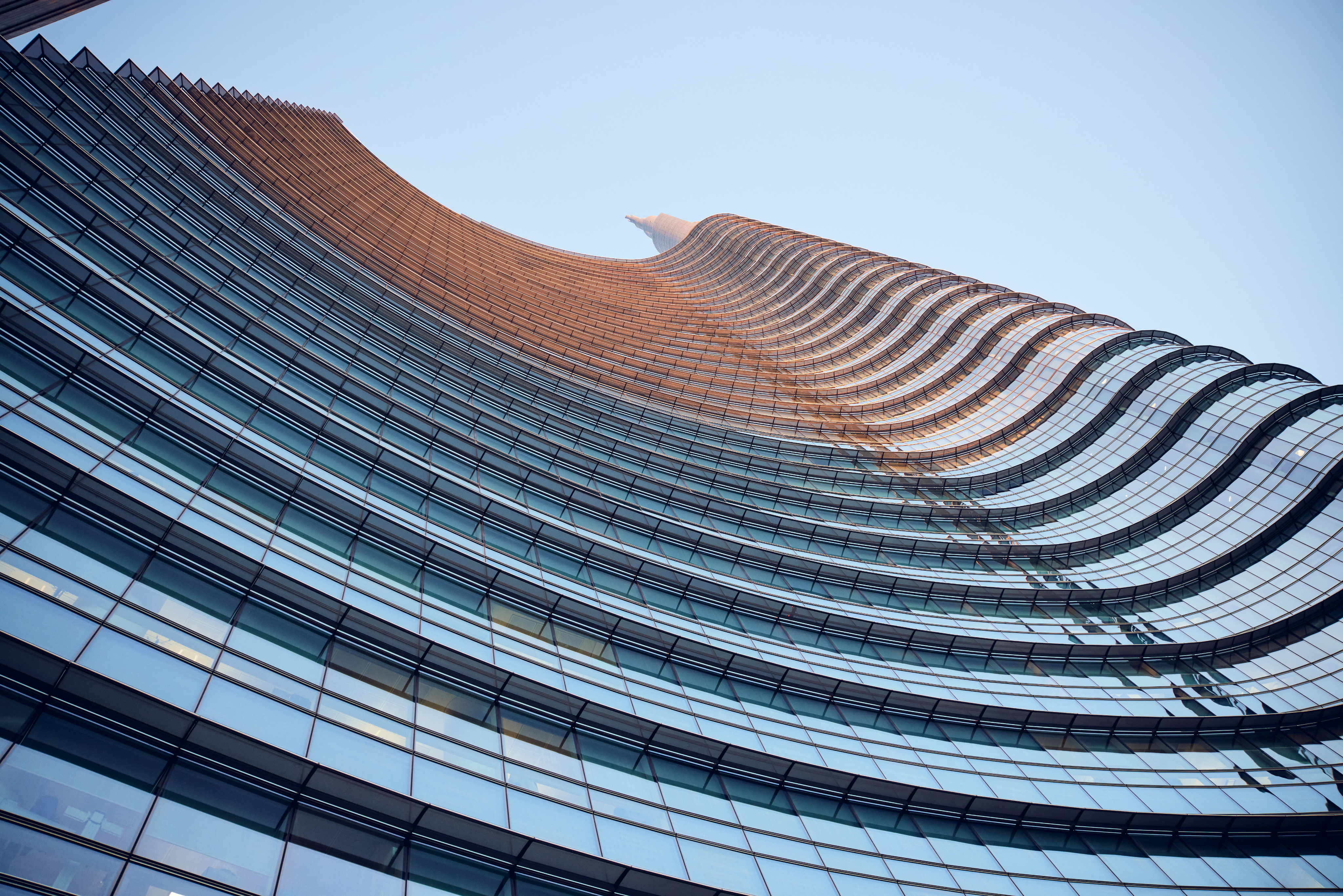 Una vista dal basso della Torre UniCredit a Milano, che mostra la sua facciata curva e stratificata.
