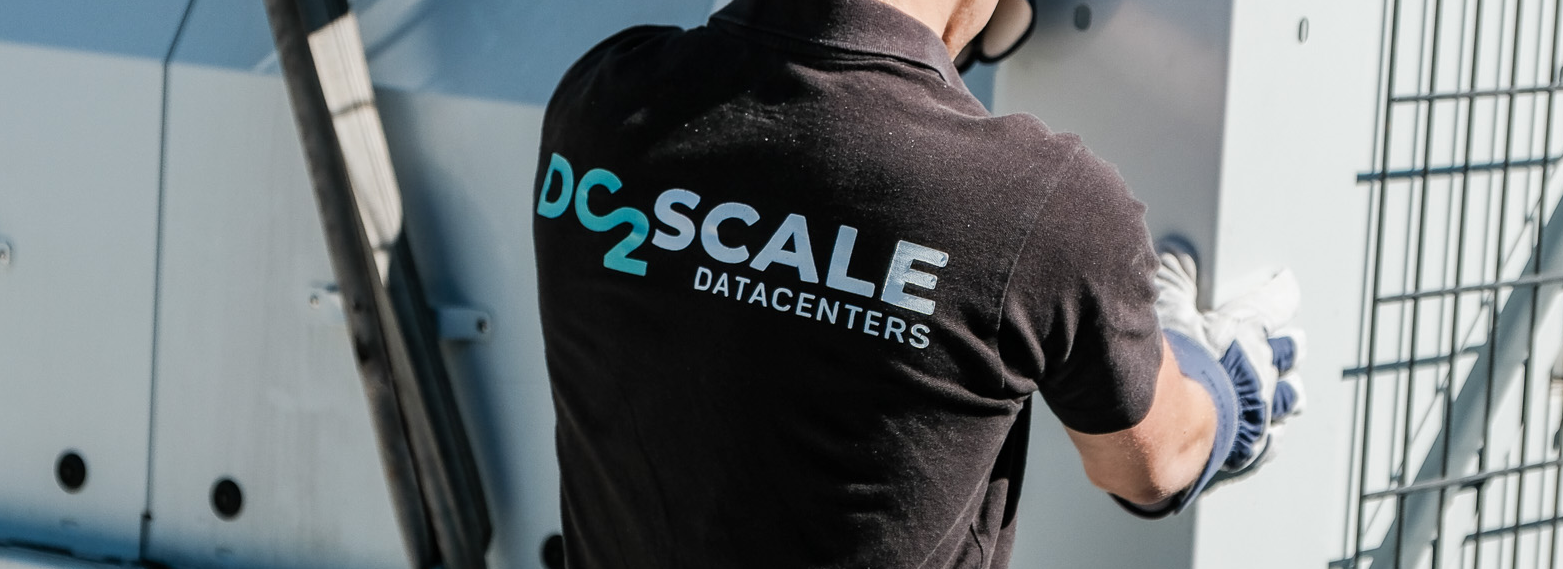 Person wearing gloves and a "DC2Scale Datacenters" shirt working near equipment outdoors.