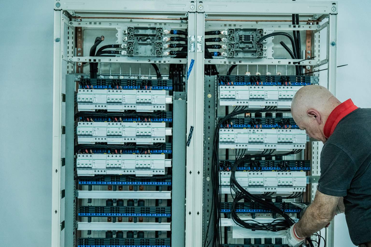 A person working on a large electrical panel with numerous wires and circuit breakers in a technical environment.