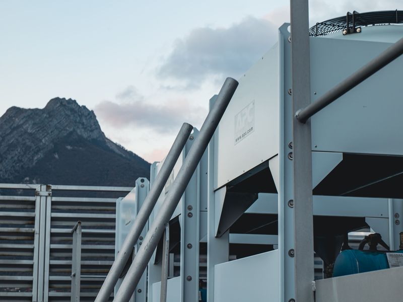 Industrial equipment on a rooftop with a mountain in the background under a cloudy sky.