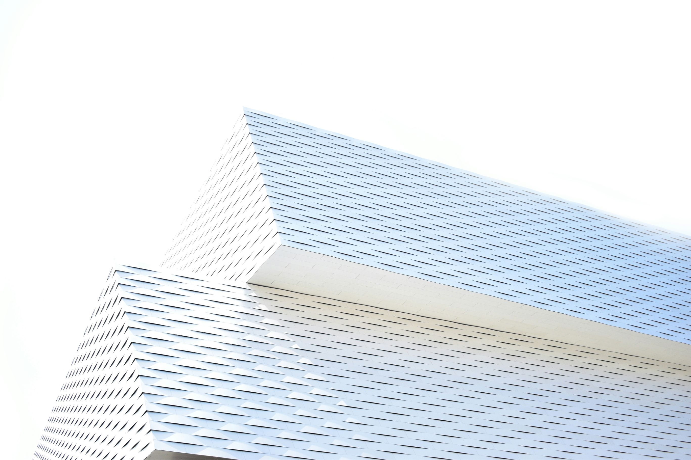 Modern architectural structure with overlapping, angled surfaces and a textured, white facade against a clear sky.