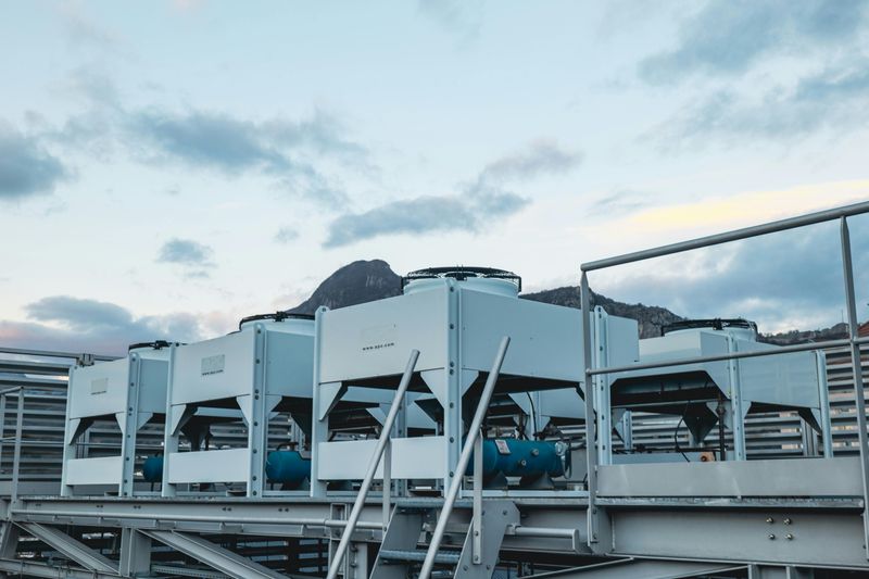 Rooftop HVAC units against a cloudy sky and distant mountains (Alps), with metal beams in the foreground. Located in the DC2SCALE ALP1 Grenoble Datacenter
