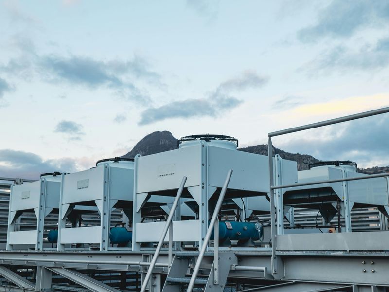 Rooftop HVAC units against a cloudy sky and distant mountains (Alps), with metal beams in the foreground. Located in the DC2SCALE ALP1 Grenoble Datacenter