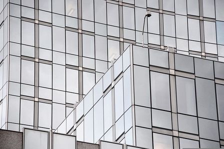 Glass building facade with reflective windows arranged in a grid pattern, featuring a geometric, modern architectural design.