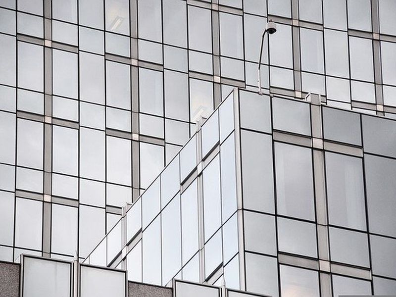 Glass building facade with reflective windows arranged in a grid pattern, featuring a geometric, modern architectural design.