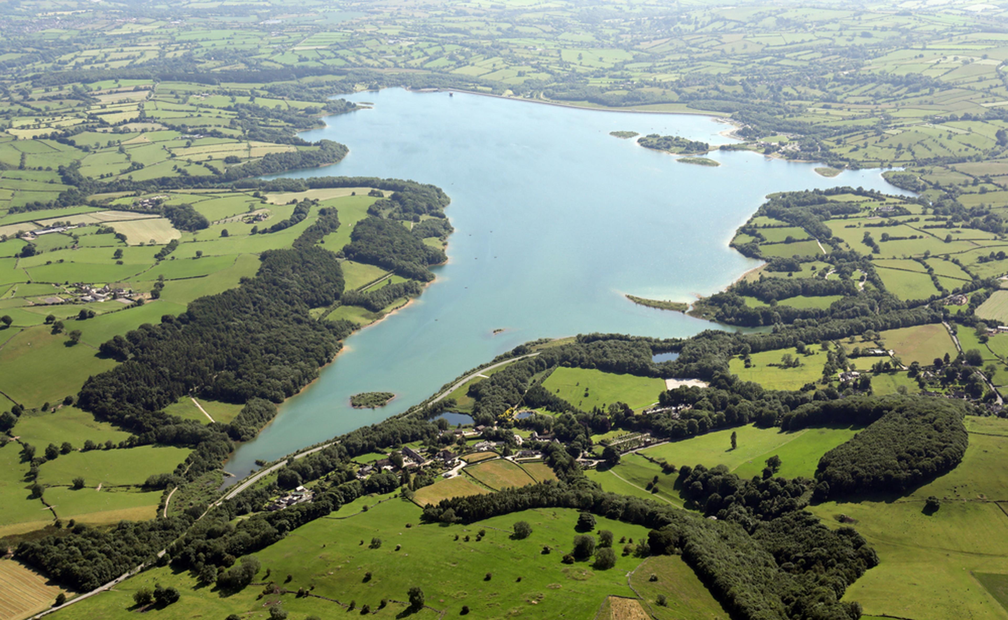 Aerial view of a large lake surrounded by green fields and patches of forest, with small settlements scattered throughout the landscape.