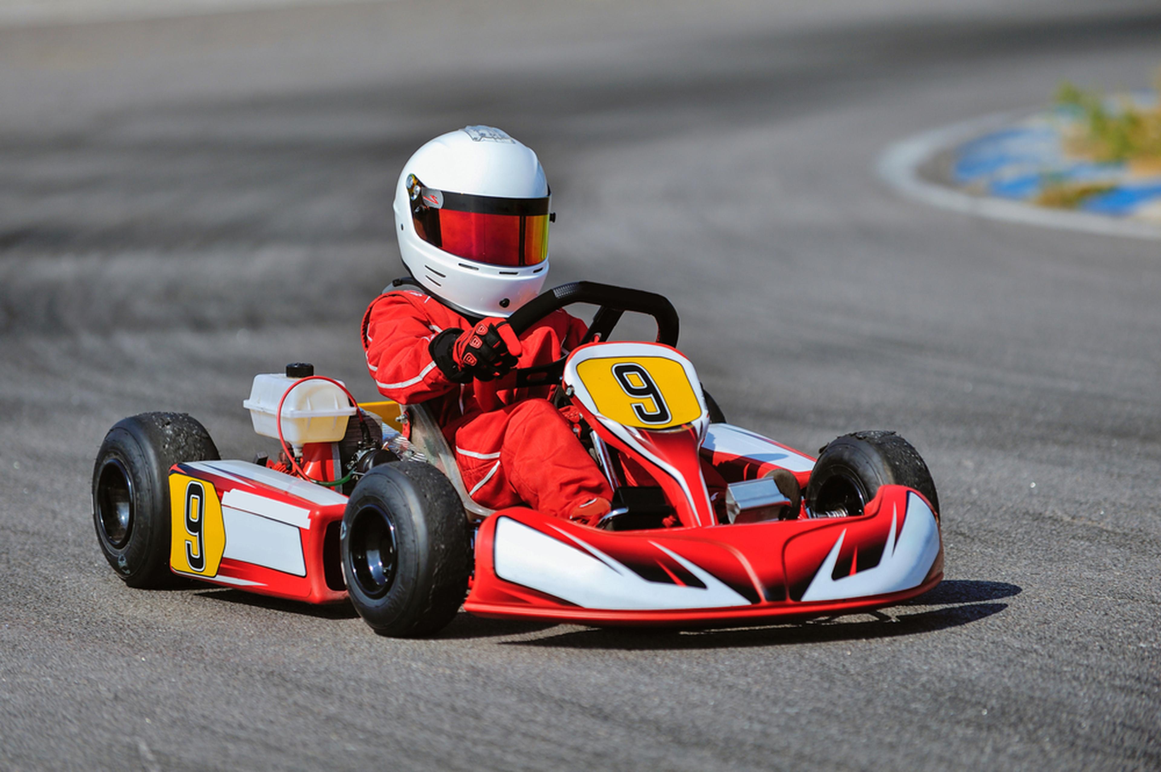 Person wearing a white helmet races a red go-kart with number 9 on a curving track