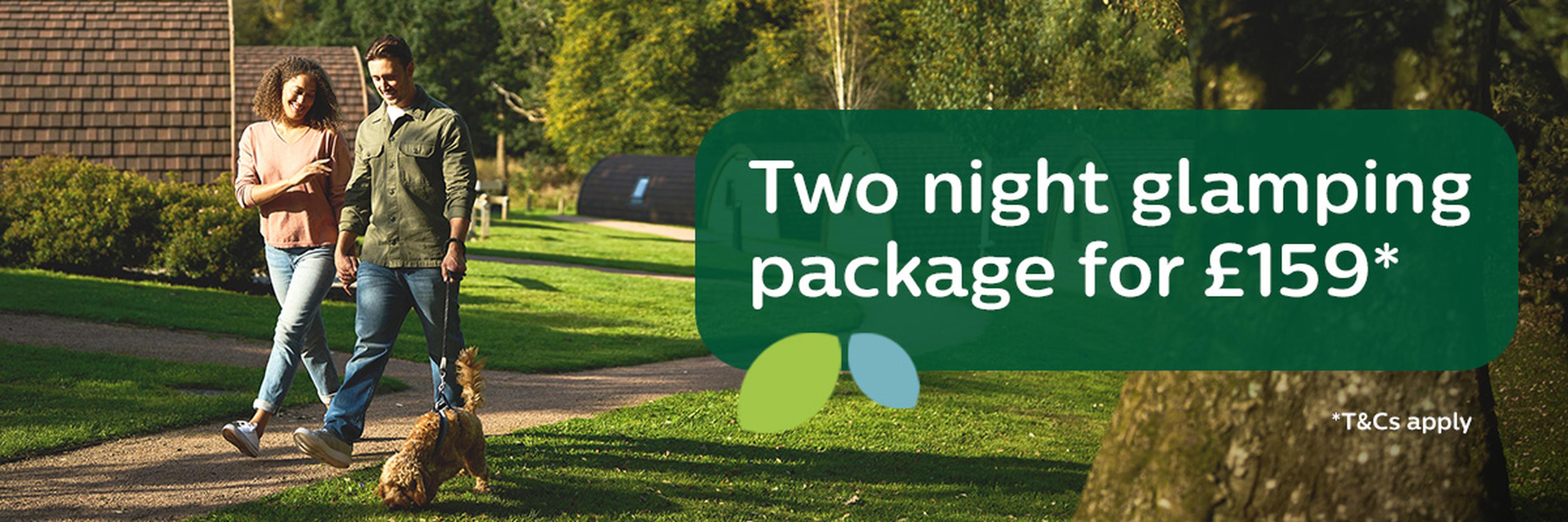 Couple walking dog in green park with cabin-style accommodations. Text: "Two night glamping package for £159. T&Cs apply."