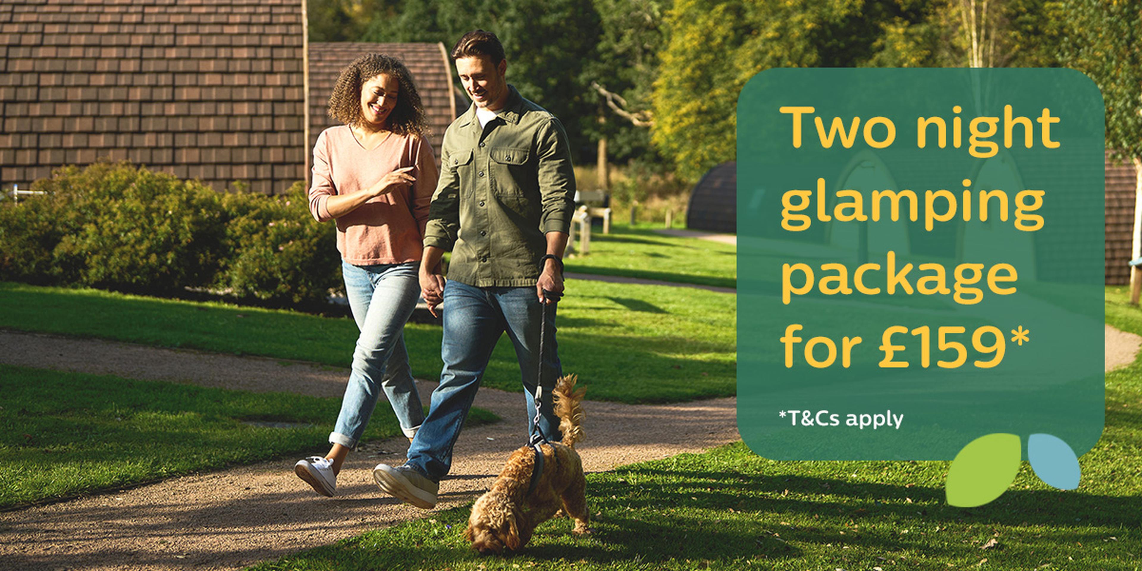 Couple walking their dog in a grassy area with glamping pods. Text: "Two night glamping package for £159* T&Cs apply."