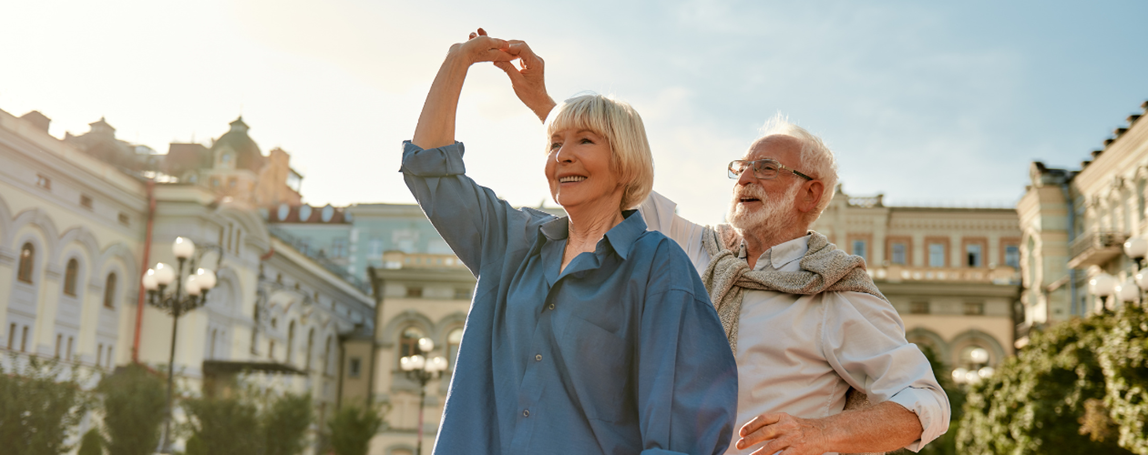 Elderly couple joyfully dancing outdoors in a scenic urban setting, surrounded by historic architecture.