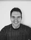 Black and white photo of a smiling person wearing a patterned sweater against a plain background.
