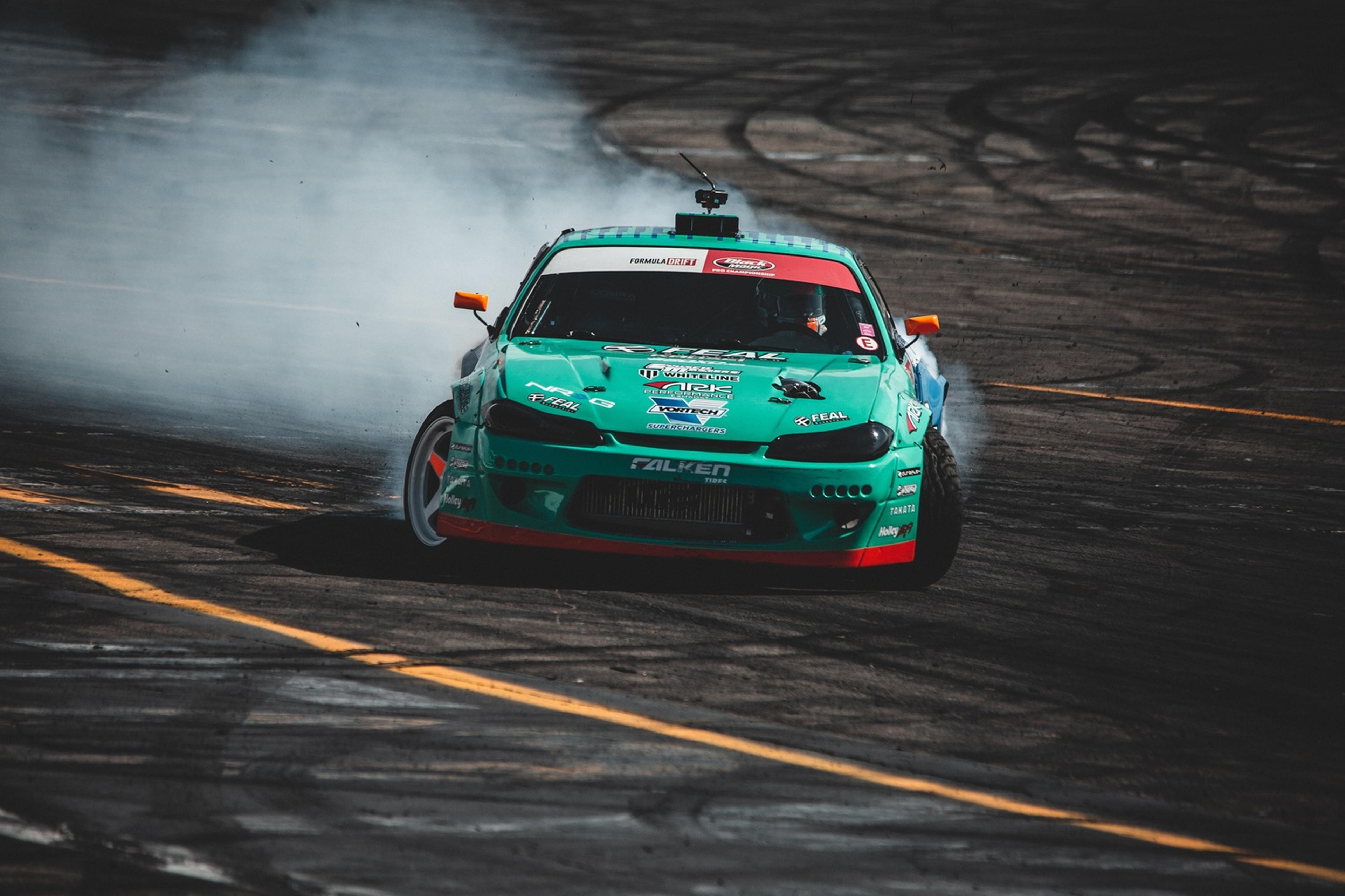 A turquoise race car drifts on a track