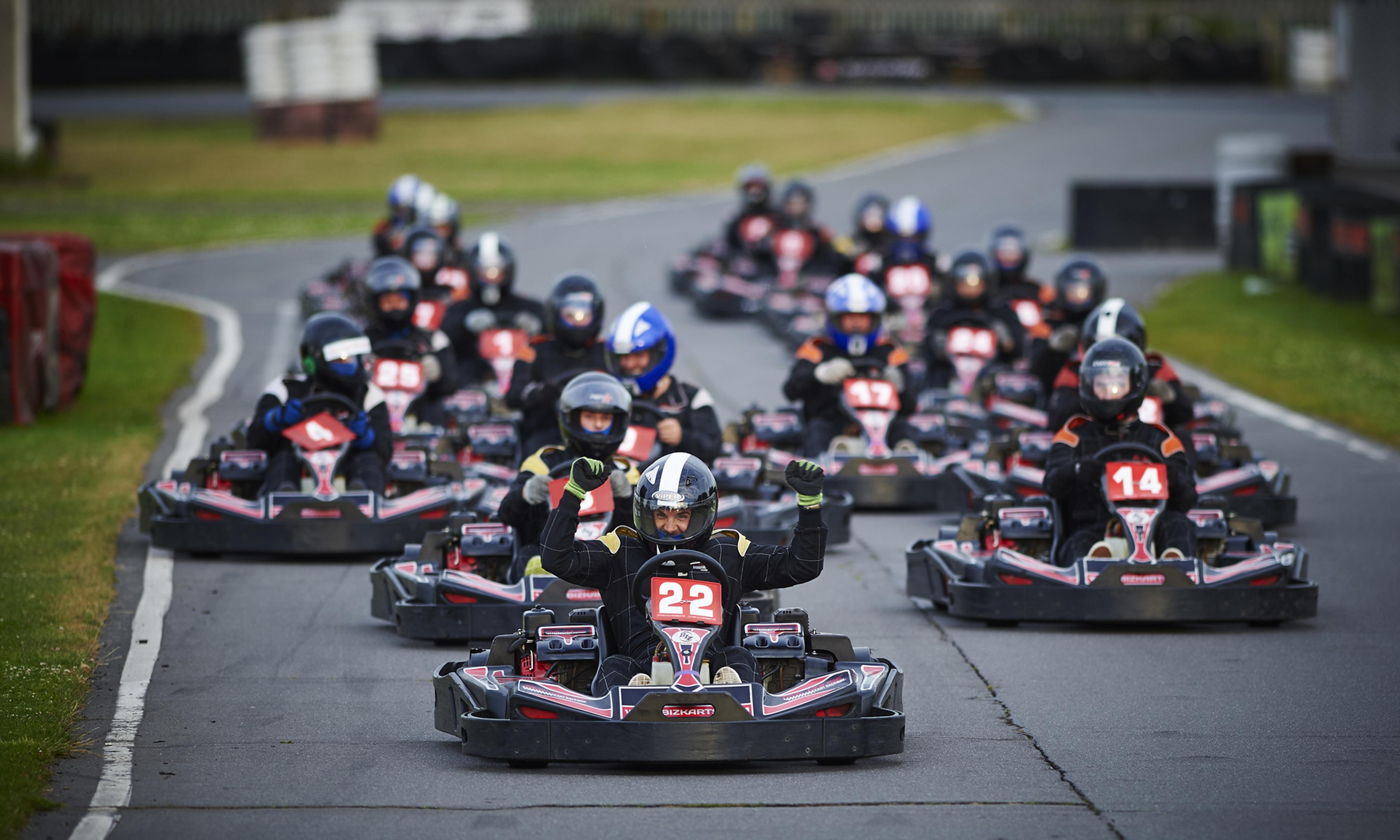 A group of go-kart racers in helmets competes on a track