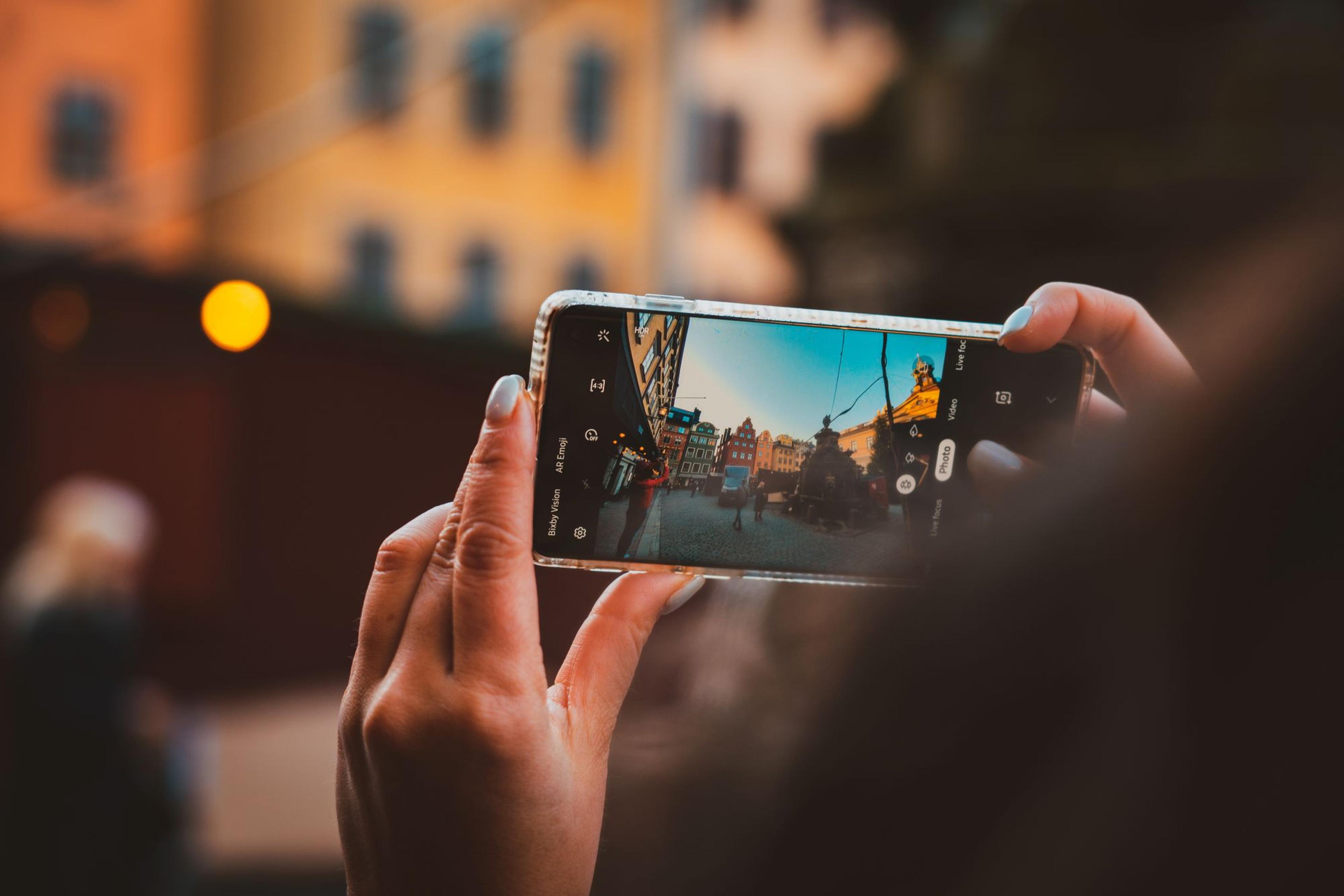 Hands hold a smartphone capturing a scenic street view with colorful buildings in the background, creating a digital memory.