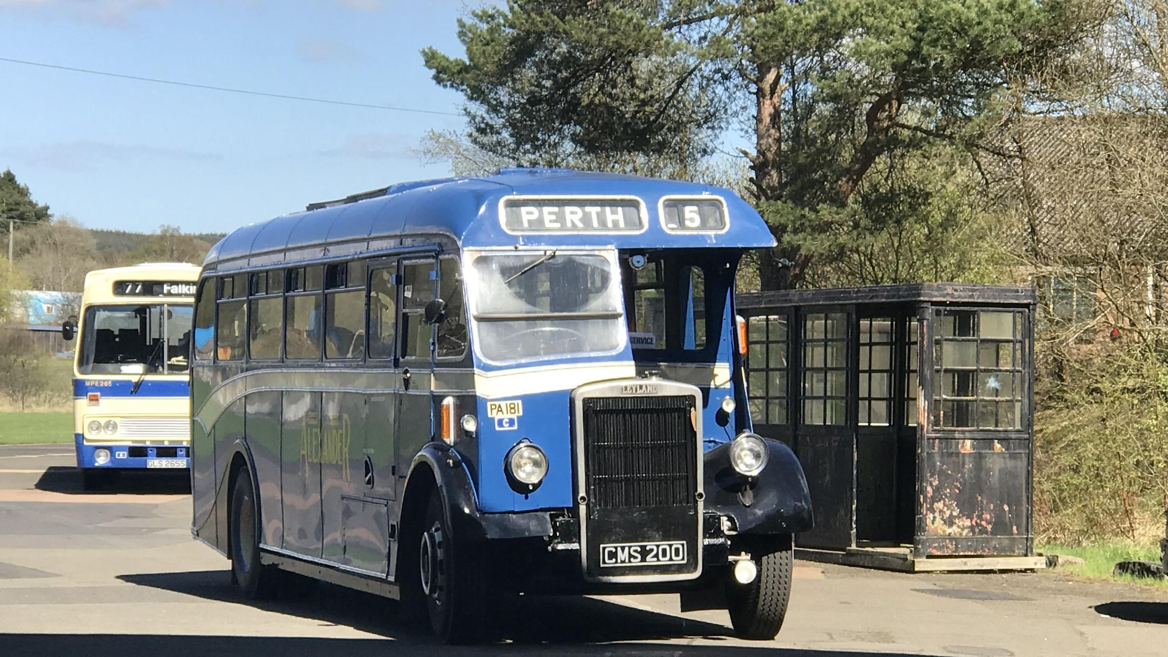Vintage blue bus labeled "Perth" next to a weathered bus stop, with another bus labeled "Falkirk"