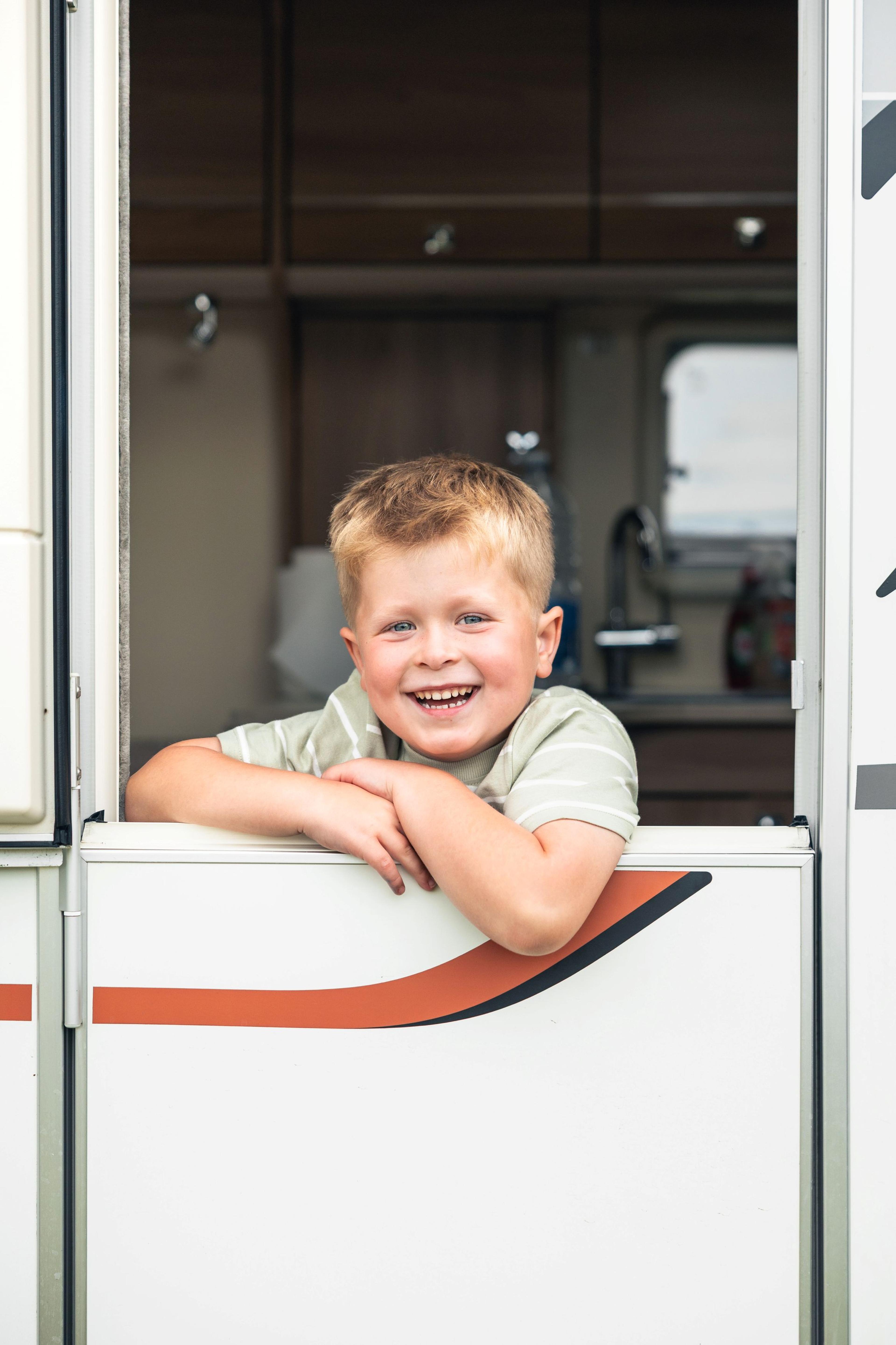 A child leaning out of a caravan door smiling