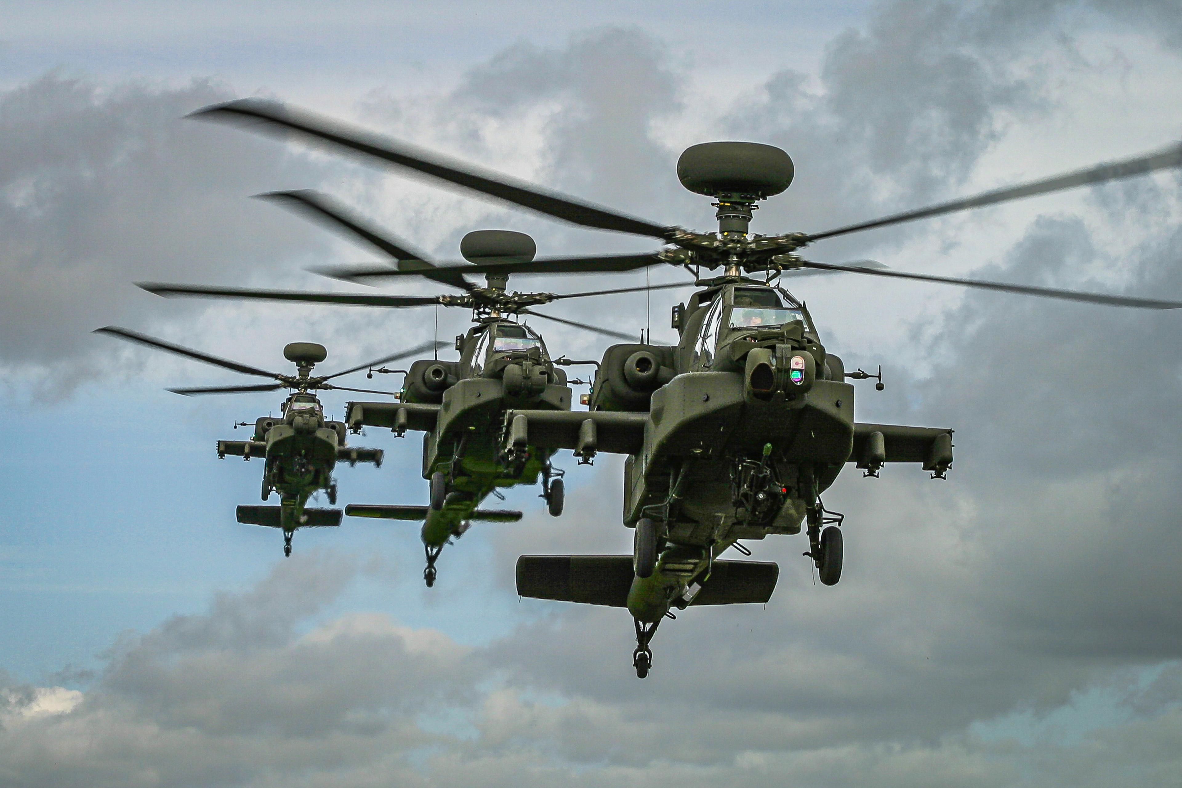 Three military helicopters flying in formation against a cloudy sky, displaying rotors and equipment.