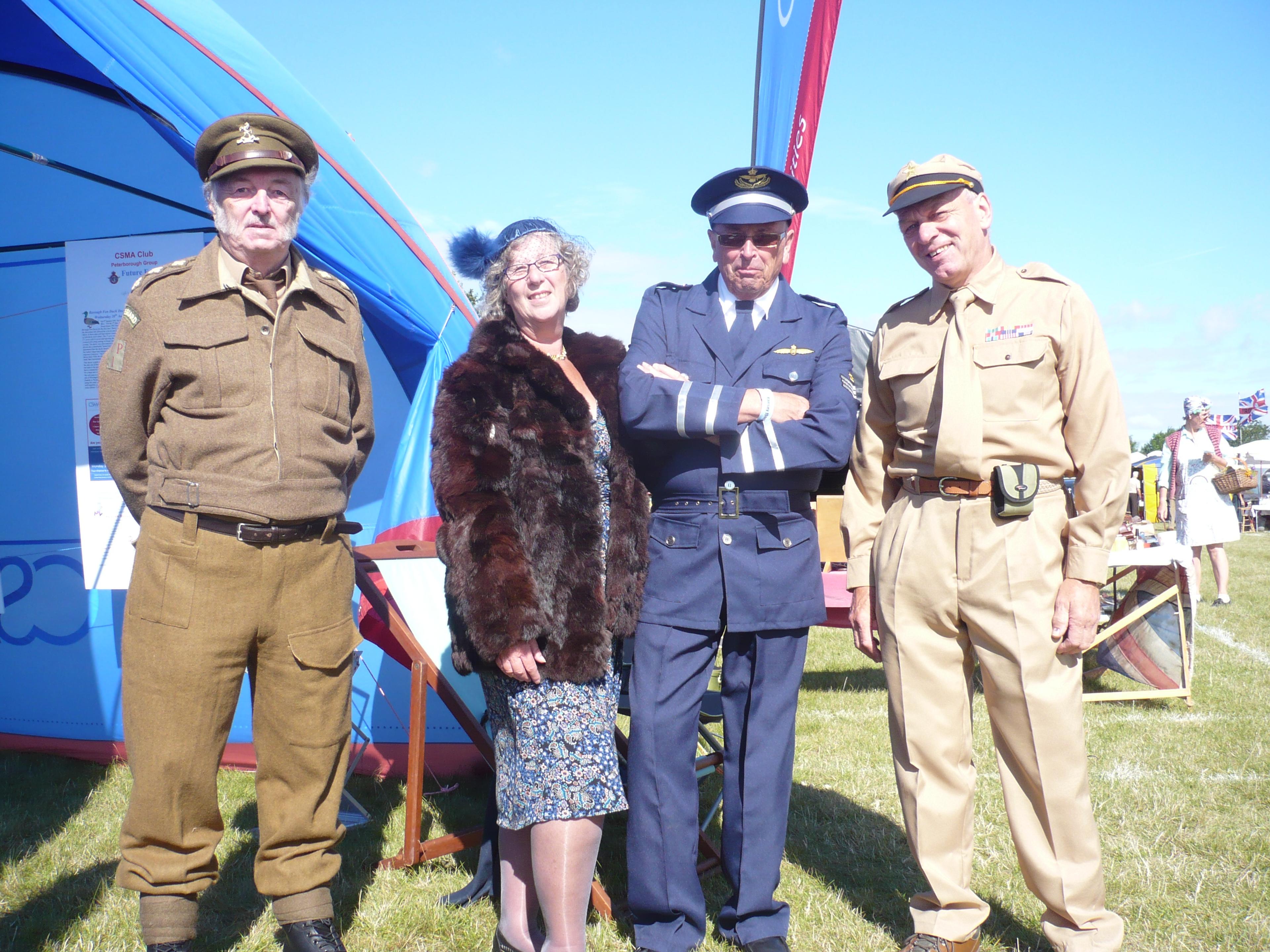 Four people in vintage military and civilian attire stand outside a tent
